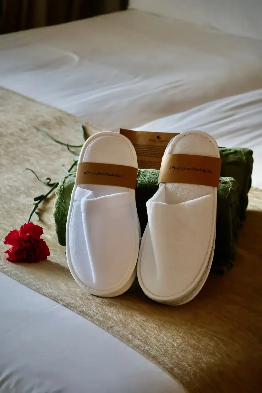 White hotel slippers and a red rose laid on a turned-down bed